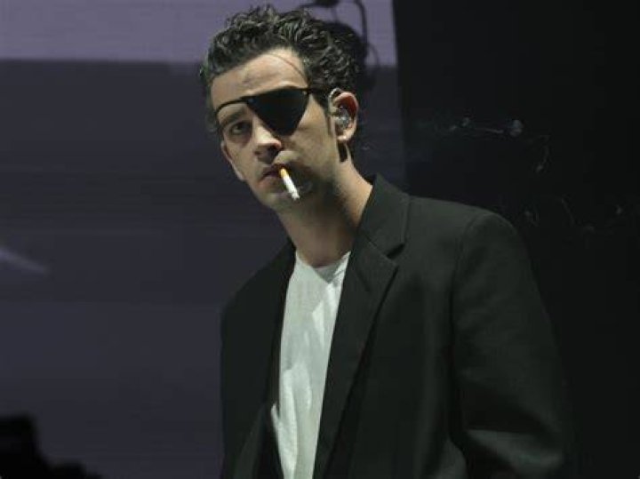 Matty Healy performs on stage at Lollapalooza Chile 2023, drinking from a bottle and smoking a cigarette